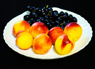 Still life of fresh fruit grapes, apples, apricots and pears on a white plate. Decorative wooden background. Ripe juicy sweet fruits. Vegetarian diet food.