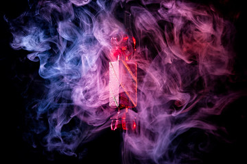 Red shiny decoration Christmas toy candy in colored violet-red smoke, on an isolated black background. Concept of a modern Christmas card.