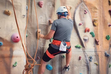 Gardinen Young man practicing rock climbing on artificial wall indoors. © herraez