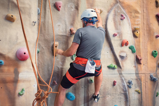 Young man practicing rock climbing on artificial wall indoors.
