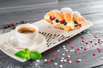 Tasty croissant with fruits and cup of coffee on the wooden background