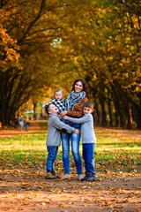 Fototapeta premium Young happy mother with her three smiling sons wearing denims and walking in the autumn park. Mom with her children on the autumn background.