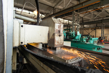 Metal parts on a flat grinder are treated with an abrasive wheel, sparks fly from under the circle, wide-angle photos.