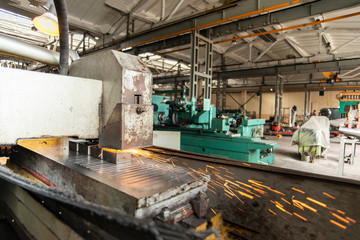 Metal parts on a flat grinder are treated with an abrasive wheel, sparks fly from under the circle, wide-angle photos.