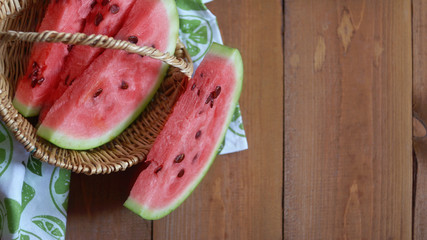 Autumn still life with a cut juicy watermelon and wedges in a wicker basket on a wooden background with a tissue napkin. View from above, cope.