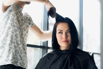 Unrecognizable hairdresser creating hairstyle for beautiful brunette woman