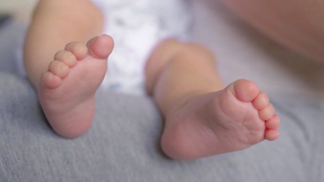 A close up of a baby naked feet. Her tiny toes are slowly moving while a baby is sitting on her parents lap