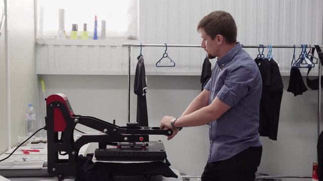 Man small business owner uses hand press to print on clothing at workshop