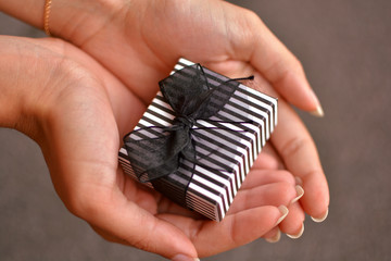 manos de mujer sujetando una bonita caja de regalo con un lazo negro mostrando una acci&oacute;n de entrega durante un posible cumplea&ntilde;os o aniversario con posiblemente alguna joya dentro
