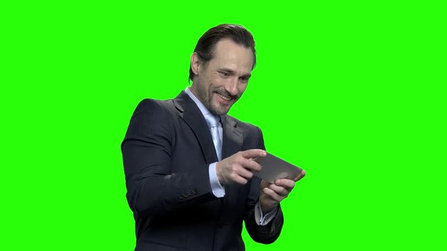 Mature excited business man plays video games on his phone. Green screen hromakey background for keying.