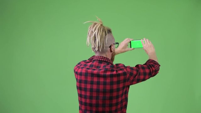 Back view of hipster man with dreadlocks taking picture with phone