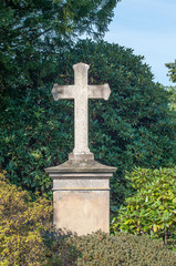 Kreuz-Grabmal auf dem Friedhof von Herdecke vor grünen Hecken aus Rhododendren