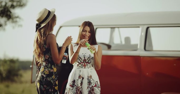 Two ladies with a good mood spending a nice time together , wearing a stylish retro dress , beside stand a beautiful retro bus. 4k