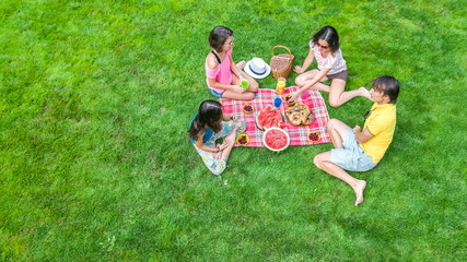 Happy family having picnic in park, parents with kids sitting on grass and eating healthy meals...