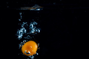 Fototapeta na wymiar bright orange tomato sinks in the dark water leaving behind a bright bubbles