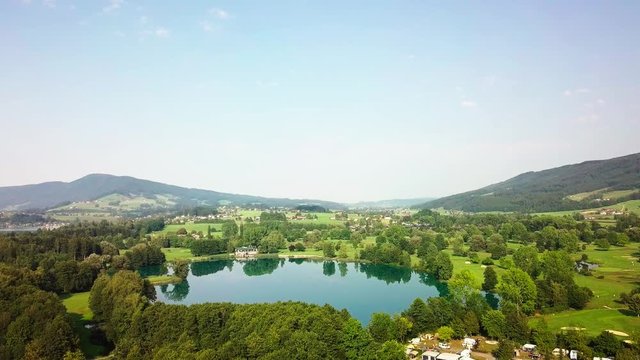 Aerial View on the mountain lake with yachts in morning time in summer sunny day under sun light. Beautiful mountains landscape view. Drone 4K Video.