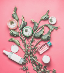 Fototapeta na wymiar Beauty background with various facial cosmetic products with mock up, leaves and green flowers on pastel pink desktop background. Modern skin care layout, top view, flat lay.