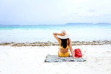 Sexy girl with yellow bikini sitting relaxed with favorite hat near the blue sea, Summer vacation of the week.