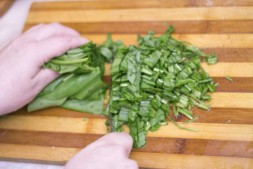 Woman cutting sorrel by knife on the wooden cooking desk