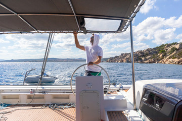 Attractive male skipper navigating the fancy catamaran sailboat on sunny summer day on calm blue...