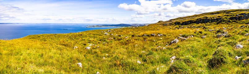 Panorama of farm field in Burren way trail with Galway bay in background