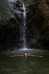 Fototapeta na wymiar Young beautiful teenage girl swimming and enjoying the waterfall