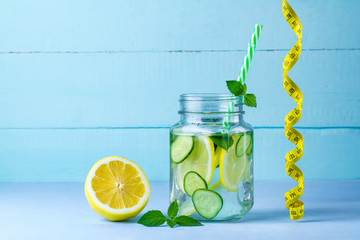 Diet concept. Detox drinks. Lemon water, juicy lemon, mint and measuring tape on a blue background.