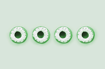 Many small plastic donuts lies on a pastel colorful background. Flat lay minimal pattern. Top view