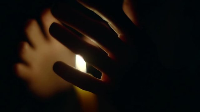 woman is warming her hands near flaming candles in darkness, moving them, close-up