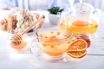Vitaminic healthy sea buckthorn tea in small glass tea pot with sea buckthorn berries and honey in the white table