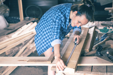 Happy carpenter woman measures a wooden Board measuring tape in the home workshop