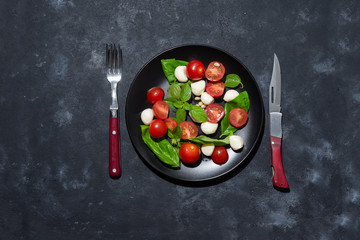 Fresh italian caprese salad with mozzarella and tomatoes on black plate over dark stone background with copy space, flat lay