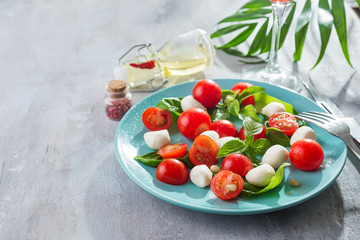 Delicious caprese salad with ripe cherry tomatoes and mini mozzarella cheese balls with fresh basil leaves on blue plate and gray slate background. Italian healthy food concept