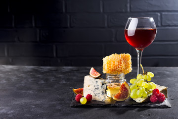 Grape, cheese, figs and honey with a glasses of red on a stone black background, copy space