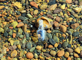 Decorative bottle on the rocks in the sea with shells. A discarded bottle floating in sea water....