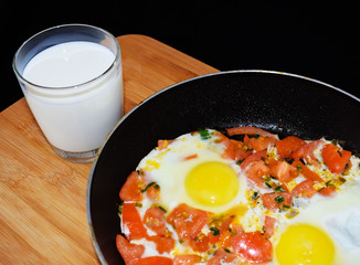 Egg with tomatoes, green onions and cheese. Glass of steamed milk. White plate on black background. Rich protein Breakfast. Food for athletes. Diet menu. Omelet with cheese for dinner. Slices of chees