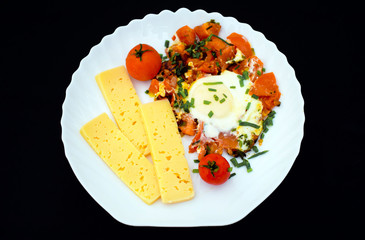 Egg with tomatoes, green onions and cheese. White plate on black background. Rich protein Breakfast. Food for athletes. Diet menu. Omelet with cheese for dinner. Slices of cheese and cherry tomatoes o