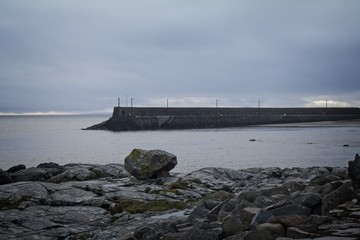 A moody view of a pier with a rocky foreground.
