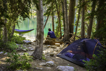 Man admiring view of a mountain alpine lake from him campsite.