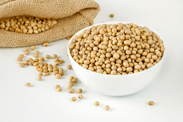 Soybeans in a white ceramic bowl and a bag on a white background. Seeds of soy.