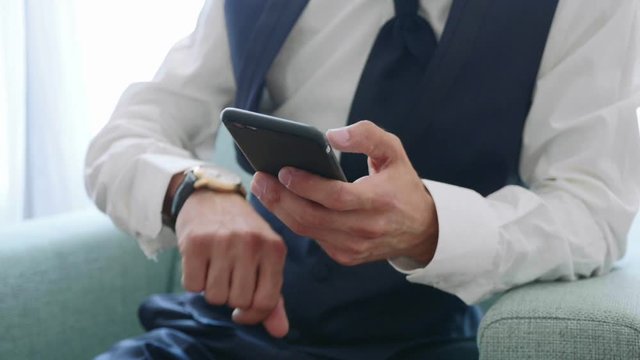 Hands with smart phone of man in suit sits on armchair