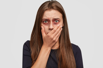 Human trafficking, abuse and hopelessness concept. Beaten up girl covers mouth, stares with eyes...