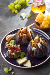 Gourmet appetizer of baked figs with goat cheese,walnuts and honey on ceramic plate and brown concrete background,