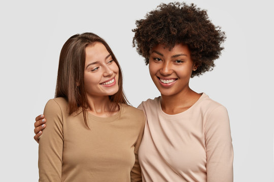 Interracial friendship and diversity concept. Delighted happy mixed race women embrace, glad to meet, express friendly relationships, isolated over white background. Multiethnic lesbians indoor.