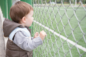 A boy 1,5 years old at the edge of a stadium watching football