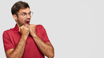 Crazy man with terrific expression keeps mouth widely opened, exclaims furiously, being puzzled by...
