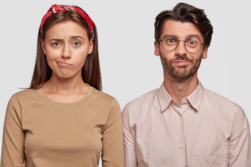 Studio shot of confused students frown faces, purse lips, cant see way out in difficult life situation, stand shoulder to shoulder against white background. Frustrated coworkes recieve task from boss