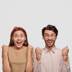 Vertical portrait of young overjoyed friendly woman and man clench fists in victory gesture, shout yes, express excitement, isolated over white studio wall with copy space for your advertisement