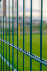 Fencing of the football field from metal with a green lawn.