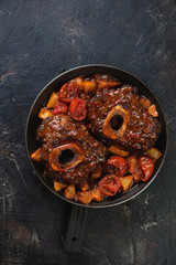 Osso buco made of cross cut veal shank with stewed oranges and tomatoes, flatlay on a dark brown stone background, vertical shot